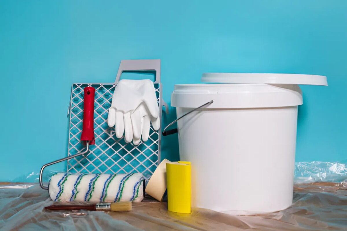 Paint prep supplies, including a roller, paint tray, gloves, brushes, tape, and a large paint bucket