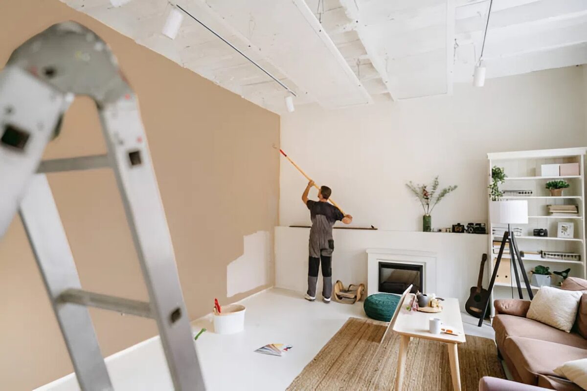 Professional painter applying warm beige interior paint with a roller in a modern living room.